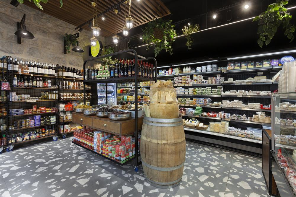 עגלת תצוגה במרכז החנות בצד חבית יין ישנה עליה גבינות קשות לת